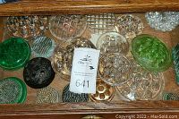Overview of different vintage flower frogs made of clear, green, uranium glass, and metal, arranged in a wooden drawer.