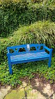 Blue wooden garden bench in outdoor setting on greenery ground with signs of wear and paint chipping.