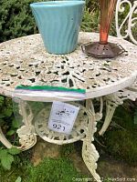 White cast iron round table top with floral cutout pattern and turquoise ceramic pot and amber feeder placed atop