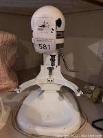 Front view of white KitchenAid stand mixer sitting on counter with auction lot sticker on body.