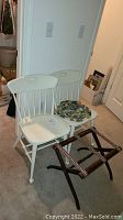 Two white ladder back chairs, one with floral cushion, placed on carpet next to wall.