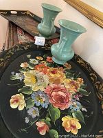 Photo showing two metal trays with detailed hand-painted floral motifs and gold painted edges along with two sage green Abingdon urns with handles.