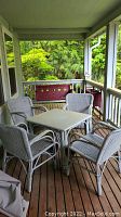 Four white wicker chairs surrounding a white wicker square table on a covered porch, red bench against railing visible