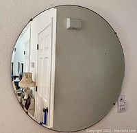 Front view of the round mirror showing its size and reflection of the room, with clear beveled edge and metal clips securing it.