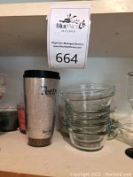 Blue Nest Home auction label with a silver Peet's Coffee travel mug and several stacked clear glass bowls on kitchen shelf.