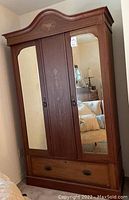 Full front view of armoire showing curved pediment, mirrored doors, center inlay panel, and bottom drawer.