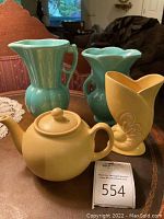 Photo of all four pottery pieces on table: two turquoise vases, yellow vase, yellow teapot, auction tag visible.