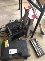 Photo showing battery charger, two car jack stands, toolbox, socket set, and car fuse package.