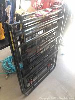 Two black metal bed risers folded and stacked, showing grid framework and metal construction.