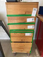 Front view of wood cabinet showing seven drawers taped shut, some drawers partially open. Drawers have wooden handles.