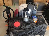 Photo of camping gear including two rolled sleeping bags, Double Quick pump, Coleman lantern in hard case with broken glass globe, Zub Zero tote, hatchet, and sharpening stone.