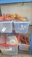 Four plastic storage bins on metal shelving, filled with tangled orange, yellow electrical cords and wires.