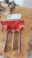 Close-up photo of large red Craftsman clamp showing clamp body, threaded screw, and two metal rods on wood surface.