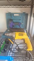 Overall lot photo showing both tools on a shelf; yellow and black DeWalt corded drill in front, purple Central Pneumatic air nailer/stapler and green carrying case behind.
