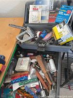 Photo showing two plastic storage containers with various tools and electrical hardware including a metal cable tacker, rolls of electrical tape, wood handled Bowie knife, bottles, and assorted small parts and tools.
