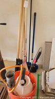 Photo of gardening tools including wooden handled post shovel, pink tool, weed sprayer, broom and flame thrower attachment.