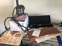 Overview photo showing the Craftsman palm grip sander resting on a box, adjacent to the Mitutoyo wooden case and sanding papers.