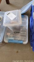 Photo of closed plastic totes on the floor containing assorted hardware items