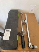 Closed black hard case labeled Pittsburgh Pro with torque wrench, handle grip, and large chrome socket on wooden surface.