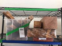 Shelving rack with a plastic tote filled with various Eastern red cedar wood blocks and pieces, large wood blocks next to the tote with one sealed in plastic packaging