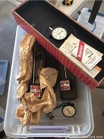 Four dial gauges and magnetic base indicators in plastic bin with red folding box.