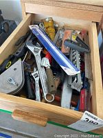 Photo showing a drawer filled with assorted hand tools including adjustable wrenches, hand saws, a putty knife, and screwdriver handles visible.