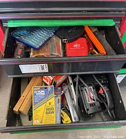 Two open drawers containing assorted hand tools, power tools and saw blades. Top drawer shows Allen wrench set, screwdriver bits, tape measure and small tools. Bottom drawer shows a Craftsman sabre saw, wooden hand saws, Bosch saw blade packaging and other tools.