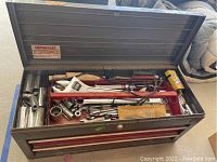 Open metal Craftsman toolbox showing removable tray with assorted hand tools inside including wrenches, screwdrivers, ratchet wrenches, sockets, hand crank, and hardware.
