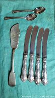 Overview photo showing all utensils laid out on cloth: 2 spoons, 4 butter spreaders, 1 serving cutting utensil