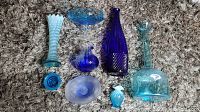 Top-down view of the assortment showing nine blue glass items including vases, bottles, and dishes arranged on carpet.