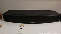 Full view of black Bose VCS-10 center channel soundbar speaker on white surface showing top and front grille with Bose logo.
