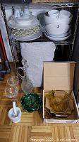 Overall view of assorted dishes, glassware, decanter, and other items on a wire shelf and floor