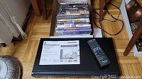 Top view of black Panasonic DVD/CD player with remote control and instruction manual on top, DVDs stacked behind.
