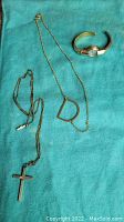 Three items on teal cloth: watch with broken band, gold filled cross necklace, and vermeil "D" necklace.