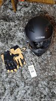 Top view of black full-face motorbike helmet and black/yellow BMX gloves on carpet.