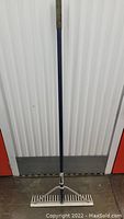 Full view of landscaping rake showing entire tool with long blue handle and metal head.