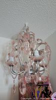 Pink glass chandelier mounted on ceiling, showing metal frame with pink glass crystals and bead strings.