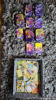 Five Pokémon card tins with various Pokémon art on the lids arranged above a gray basket with loose cards inside, all set on carpet.