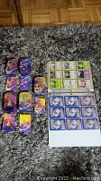 Photo showing 5 Pokemon tins with colorful character art, multiple cards laid out including art cards and card backs, all on carpet.