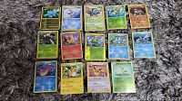 Photo showing 15 Pokemon cards arranged in 3 rows on a carpeted surface, some identified as holofoil and reverse holofoil cards from 2006 to 2014 sets.