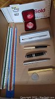 Lot overview showing pens, coins, rulers in a box