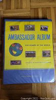 Yellow and blue Ambassador Album cover labeled for world stamps, showing some stain marks.