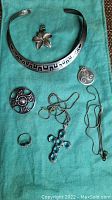 Full view of all silver jewelry items on turquoise cloth including cuff bracelet, flower pendant, round pendant, ring, cross necklace, and chain necklace