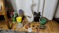 Photo showing entire assortment of decor items on floor including white art glass swan, ceramic rooster, wooden ram, vases, figurines, small wooden pieces