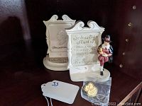 Two white miniature signs by Sebastian Studio, one with small figurine, displayed on shelf with price tag