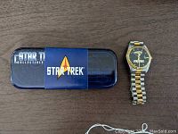 Full view of the blue Star Trek collectible tin with logo band wrapped and the two-tone gold and silver Star Trek wristwatch beside it.