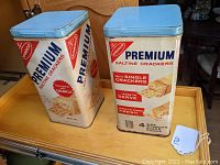 Photo of two vintage Nabisco Premium Saltine Crackers tins with blue lids showing front and side branding and design.
