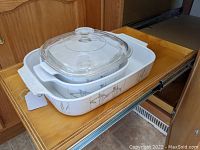 Three CorningWare casserole dishes stacked in a drawer, showing sizes and glass lids.
