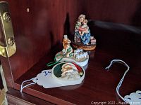 Three Sebastian miniature sculptures displayed on a wooden shelf: Madonna of the Chair, shepherd with sheep, and Santa Claus ornament with tag labeled 34.