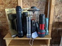 Photo of assorted flashlights and lantern-style light on a wooden surface showing various sizes, colors, and styles.